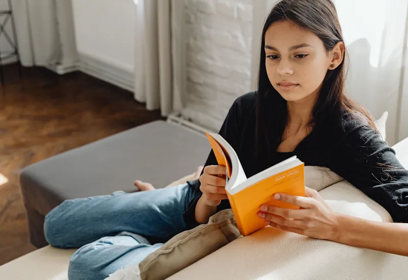 Person reading an open book on a sunlit couch.