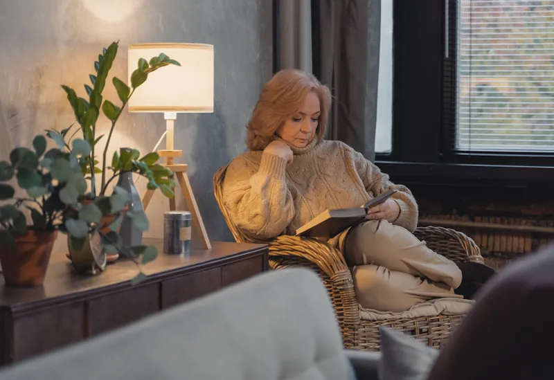 A person reading a book in a cosy lamp-lit living room