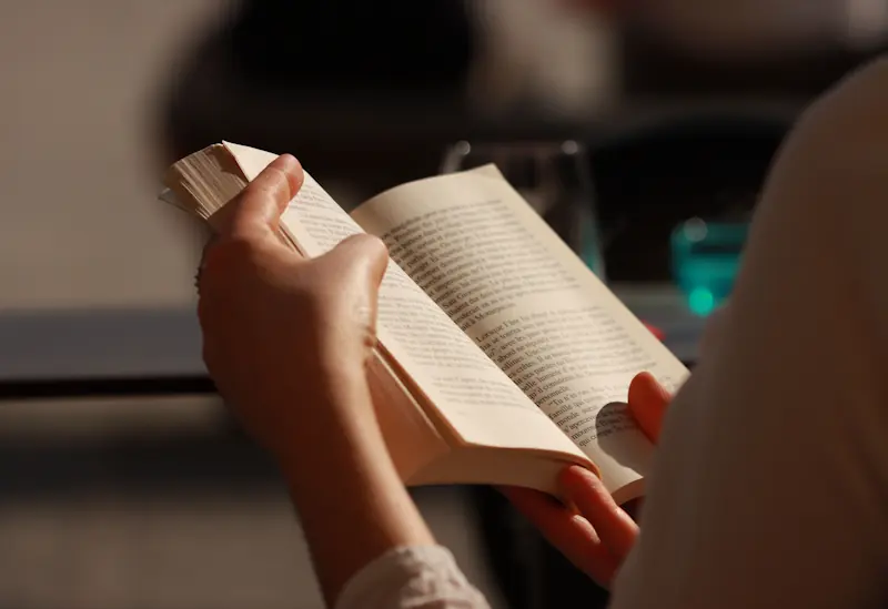 A person holding an open paperback book in warm natural light