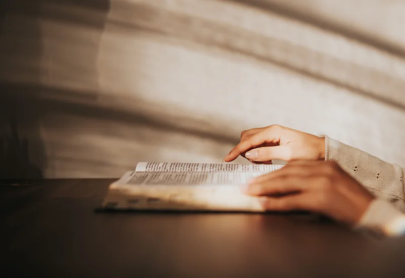 Hands resting on an open book in warm natural light on a wooden table