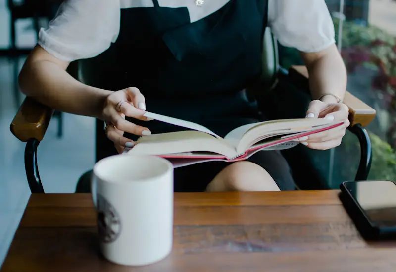 Person reading an open book at a table in natural light.
