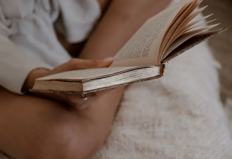 A person reading an old, worn book with yellowed pages in a cosy indoor setting