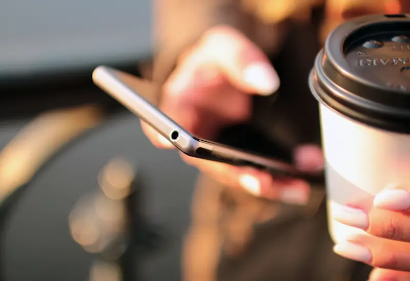 Person holding a takeaway coffee and smartphone, representing how to save money without giving up the things you enjoy.