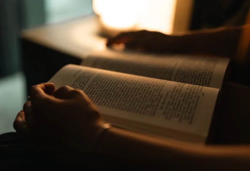 A person holding an open book in warm dim lamp light