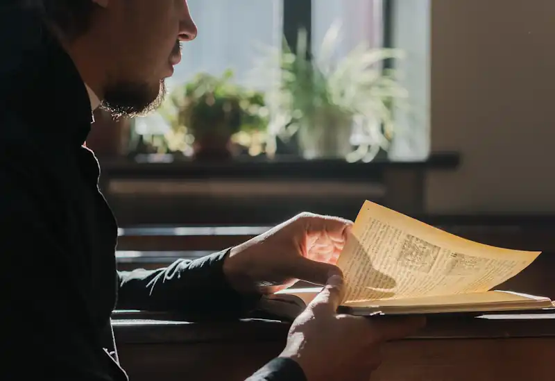 Person reading an open book at a sunlit wooden desk.