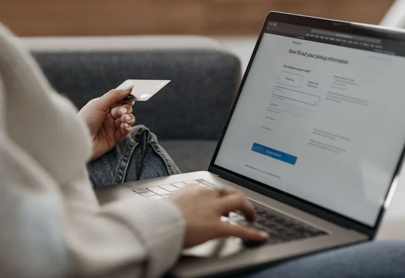 A person holding a credit card while viewing an online checkout screen on a laptop