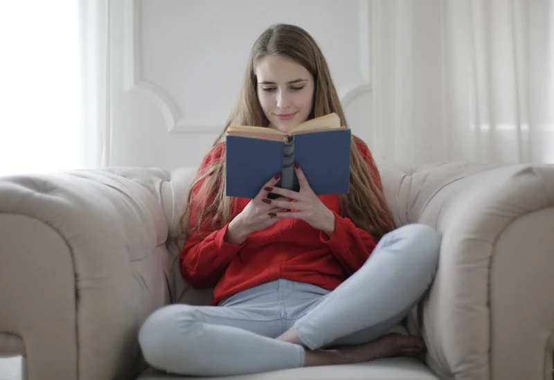 A person reading a book while sitting on a cosy sofa in soft natural light