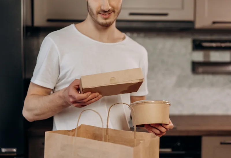 Person holding meal kit containers and a delivery bag in a kitchen, representing how to judge value for money.